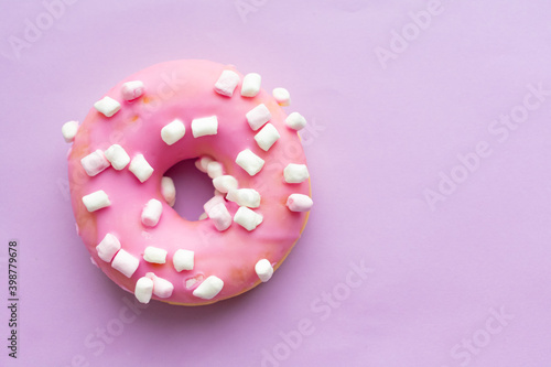 Pink sweet donut with marshmallows on a lilac background. Close-up. Flatley. Place for text and design.