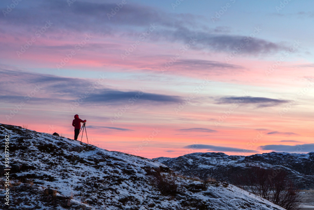 The photographer stands on a mountain against the background of the sky and takes a picture using a tripod. Bright dawn.