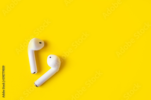 Wireless white headphones on a yellow background, place for text. Colorful summer concept