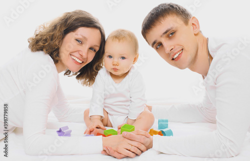 Family portrait of happy smiling mother, father playing on the floor with baby over a white background