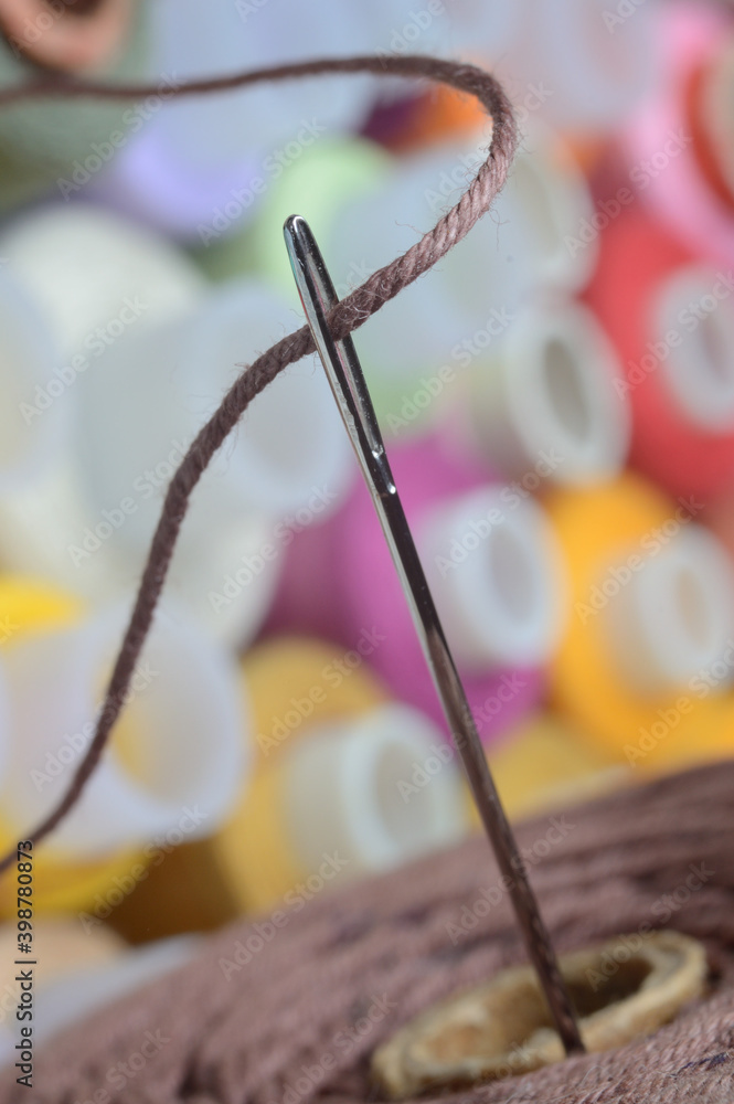 a sewing needle with brown thread through the eye of the needle. macro. a sewing needle with brown thread through the eye of the needle. macro.