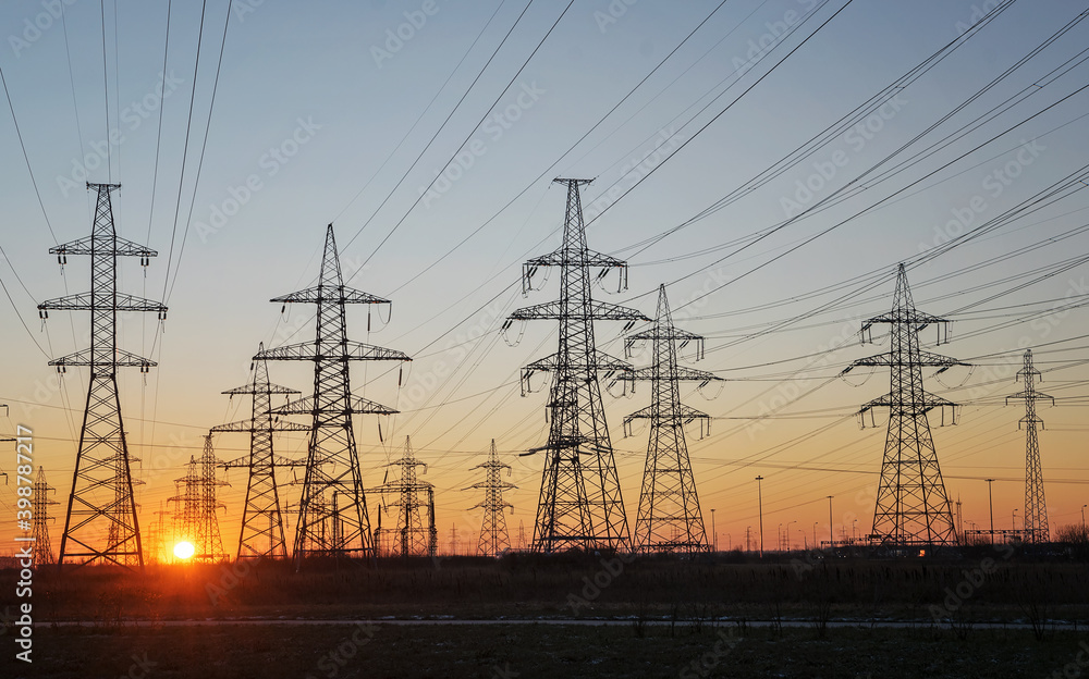 Silhouettes of a high-voltage electric tower against the background of the rising sun and sky. Selective focus.