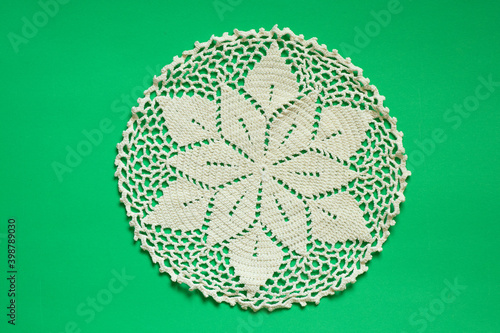 light knitted round lace doily on a green background close up