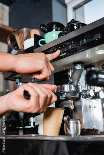 cropped of barista pushing button on coffeemaker while preparing coffee to go