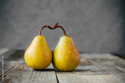 A couple of Fresh yellow ripe organic yellow pears form the shape of the heart on rustic wooden table on the gray stone background. Relations, love concept. Trend Colors of the year 2021. Copy space.