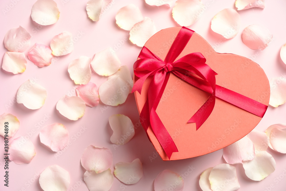Heart shaped box with red ribbon bow and white roses petals on pink table, top view. Happy Valentines Day, Mothers Day, birthday gift. Love, romance concept. Heart shaped box with red ribbon bow and white roses petals on pink table, top view. Happy Valentines Day, Mothers Day, birthday gift. Love, romance concept.