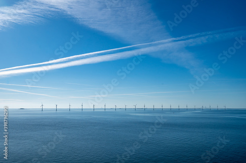 Wind turbines in the ocean with vapour trails overhead in the vast blue sky. Baltic Sea