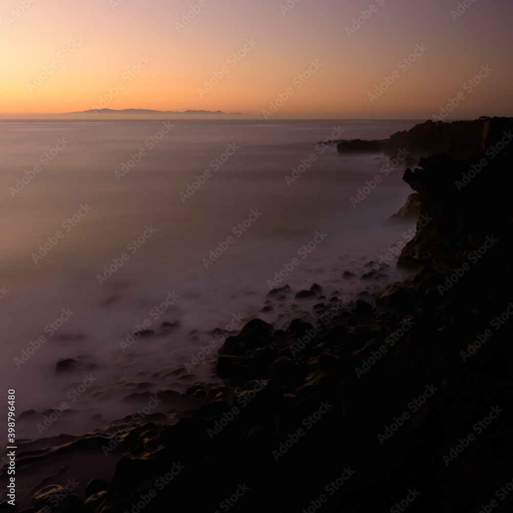 Coastal landscape long exposure photography of the sunrise in a rocky cliff in Candelaria, Tenerife, Canary Islands, Atlantic Ocean. Silk effect on water.