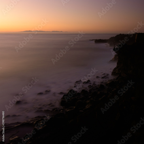 Coastal landscape long exposure photography of the sunrise in a rocky cliff in Candelaria, Tenerife, Canary Islands, Atlantic Ocean. Silk effect on water.