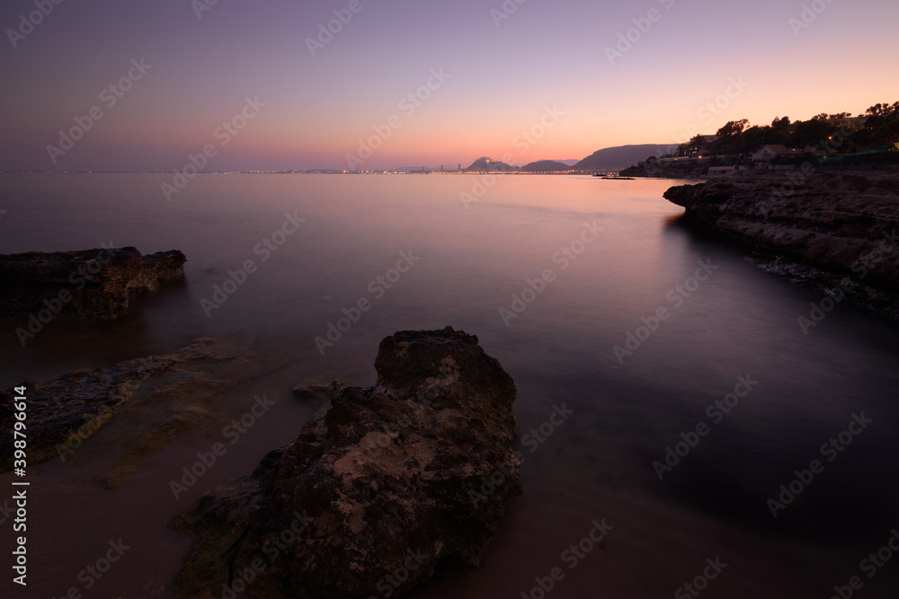 Obraz premium Coastal, sunset, long exposure landscape. Purple and red lights. Alicante harbour, Comunidad Valenciana, Spain. Cala Cantalar, San Juan.