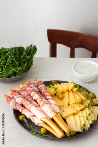 Grissini bread with bacon, several types of cheese and pea sprouts, sauce and spinach closeup on a white wooden background