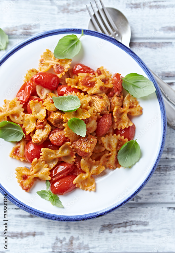 Farfalle pasta with chicken breast, cherry tomatoes and fresh basil. Bright wooden background. Top view. Farfalle pasta with chicken breast, cherry tomatoes and fresh basil. Bright wooden background. Top view.