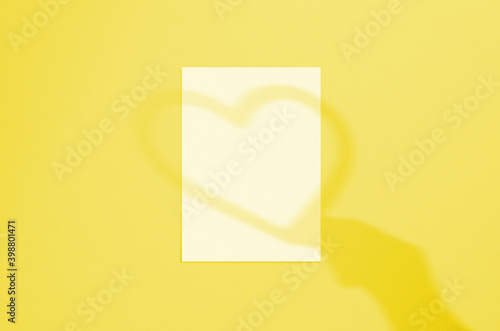 Blank white vertical paper sheet 5x7 inches with hand and heart shadow overlay. Illuminating Pantone Color Of The Year 2021. Modern and stylish valentine greeting card or wedding invitation mock up.