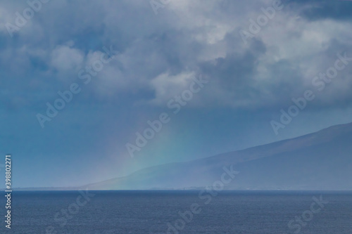 Colorful faint rainbow acdross the ocean and Molokai seen from Maui.