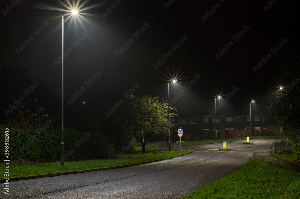 Night time image of suburban street with roundabout and street lights.