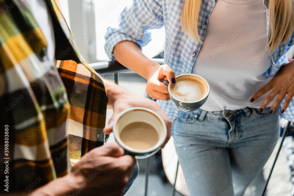 cropped of man and woman holding cups with cappuccino in cafe
