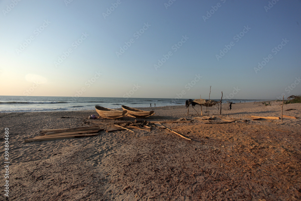 wide angle horizontal photography of a pink and blue sunset over Atlantic ocean shore, with sandy beach, wooden boats and a fishermans shelter, outdoors in the Gambia, Africa