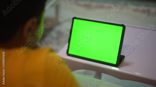 A teenage boy is watching a tablet green screen.