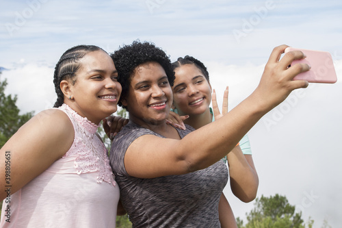 three attractive adventurers Latin American girls outdoors casual dressed smiling taking selfie with smart phone during vacation trip in dominican republic in summer day photo
