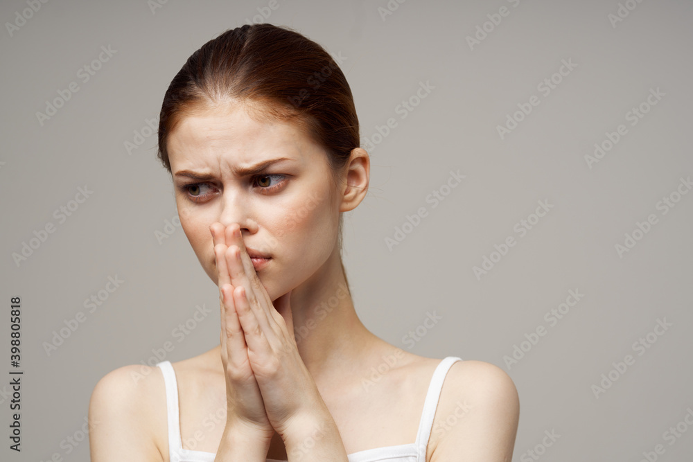 beautiful woman in a white t-shirt on a gray background joined hands near the face beautiful woman in a white t-shirt on a gray background joined hands near the face