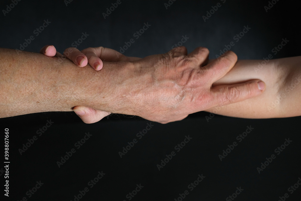 Fototapeta premium male and female hands together on black background, old skin with wrinkles and veins, concept of health, age-related changes, love, tender relationship of a couple in life