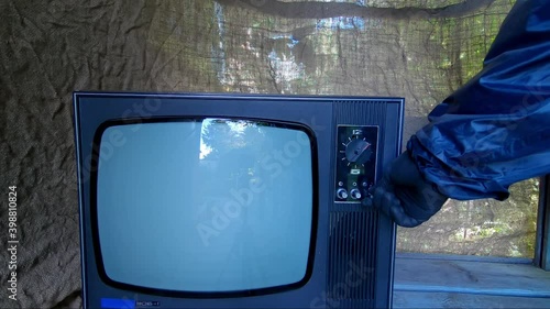 Hand in protective suit and glove turns on an old, retro TV. Device does not turn on and hand hits. There interference on TV, person switches channels