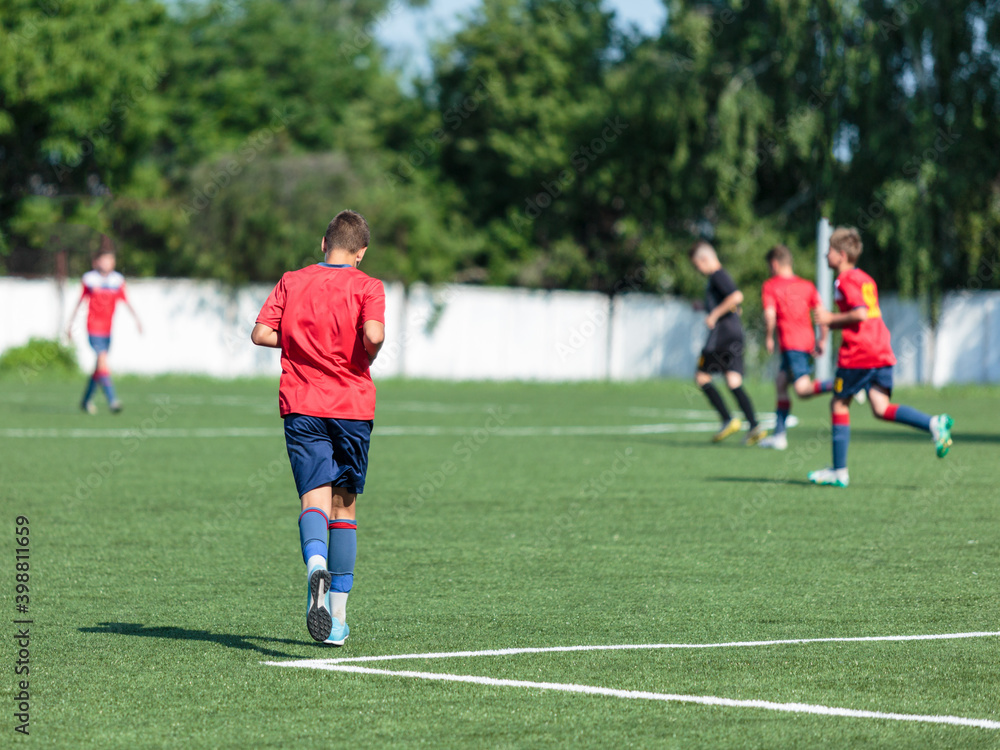 Boys in red sportswear plays football on field, dribbles ball. Young soccer players with ball on green grass. Training, football, active lifestyle for kids	