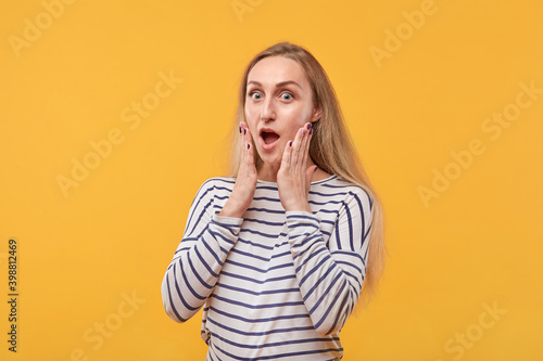 A surprised young woman looks at the camera with her mouth open. Yellow background.
