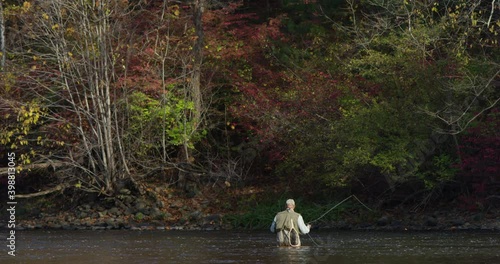 A man flyfishing waist deep in the middle of a big river and autumn foliage in background, shot in slow motion