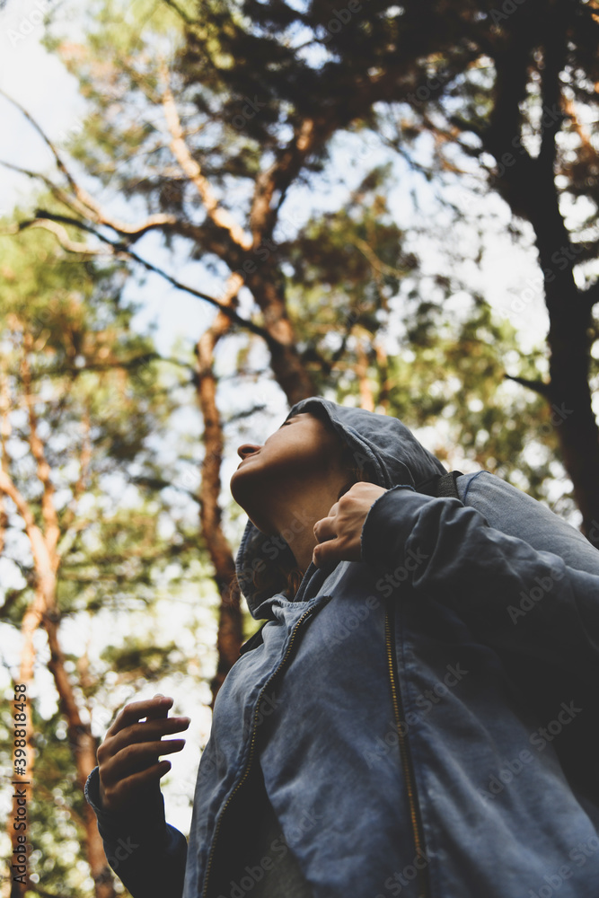 Tourist wearing in jacket with a hood at evergreen pine forest. Travel, ecotourism, ecology, local tourism, success concept, natural background with coniferous trees and an explorer in hoodie Tourist wearing in jacket with a hood at evergreen pine forest. Travel, ecotourism, ecology, local tourism, success concept, natural background with coniferous trees and an explorer in hoodie