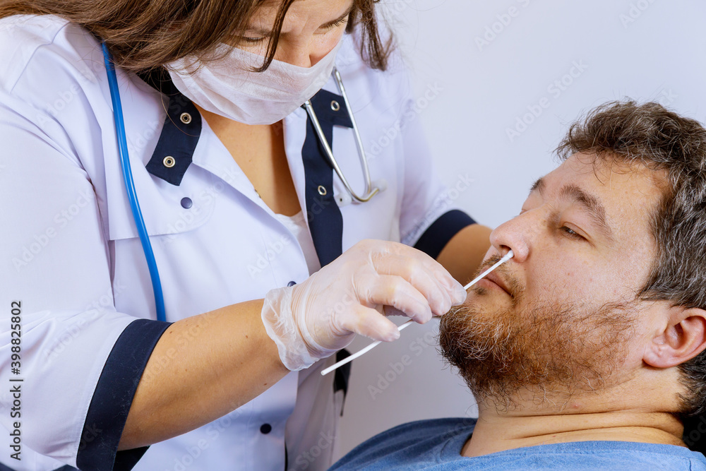 Fototapeta premium Female medical worker taking a swab for coronavirus sample plr test from potentially infected man with surgical face masks personnel taking nasal sample