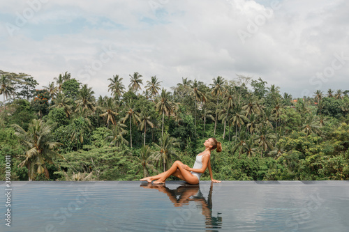 Happy woman enjoying warm sunny day in the infinity pool with a jungle view in Ubud, Bali
