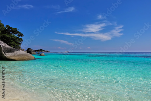 Clean, transparent Andaman Sea. Sand beach. Picturesque boulders rise above the water. Azure sky with beautiful clouds. A speedboat rushes on the horizon. Summer day in Thailand. Similan Islands.