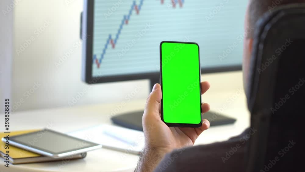 Over The Shoulder View Man at Home Sitting on a Chair Using with Green Mock-up Screen smartphone in Vertical Mode. Male Using Touchscreen Device, Browsing Internet, Watching Content Over The Shoulder View Man at Home Sitting on a Chair Using with Green Mock-up Screen smartphone in Vertical Mode. Male Using Touchscreen Device, Browsing Internet, Watching Content