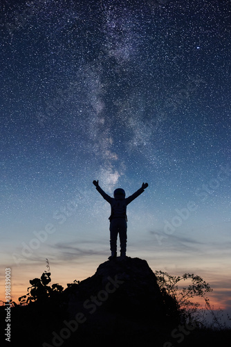 Billede på lærred Vertical shot of space traveler standing on rocky hill with night beautiful sky and Milky way on background