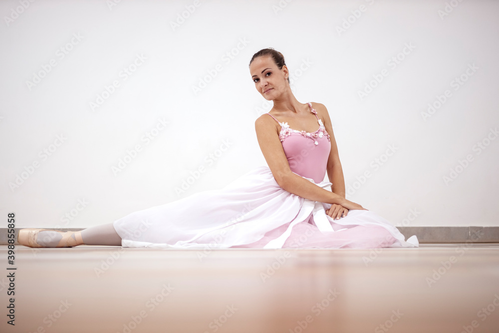 Beautiful professional ballerina in pink dress in sitting position on wooden floor in ballet studio Beautiful professional ballerina in pink dress in sitting position on wooden floor in ballet studio