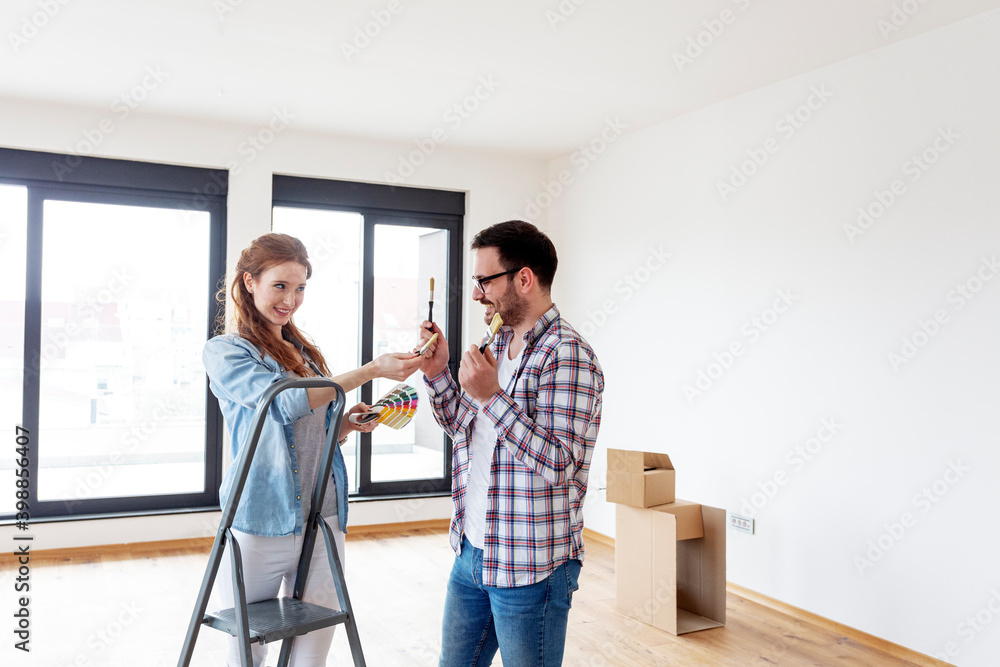 Couple in new house plan how to paint walls and looking at samples of colours with brushes on hand