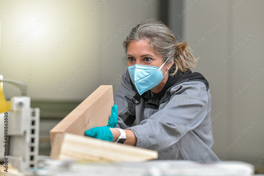 Woman worker operating on a woodworking machinery and wearing protections againt covid-19