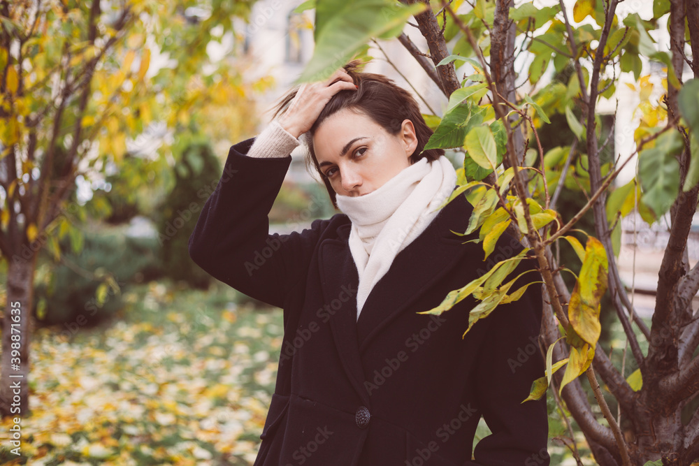 Outdoor portrait of woman in park wearing winter black coat and white scarf.
Outdoor portrait of woman in park wearing winter black coat and white scarf.