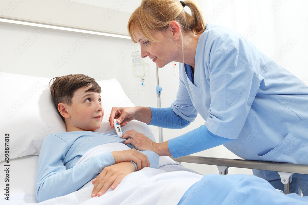 Happy child lying in bed in hospital room and nurse taking his temperature Happy child lying in bed in hospital room and nurse taking his temperature
