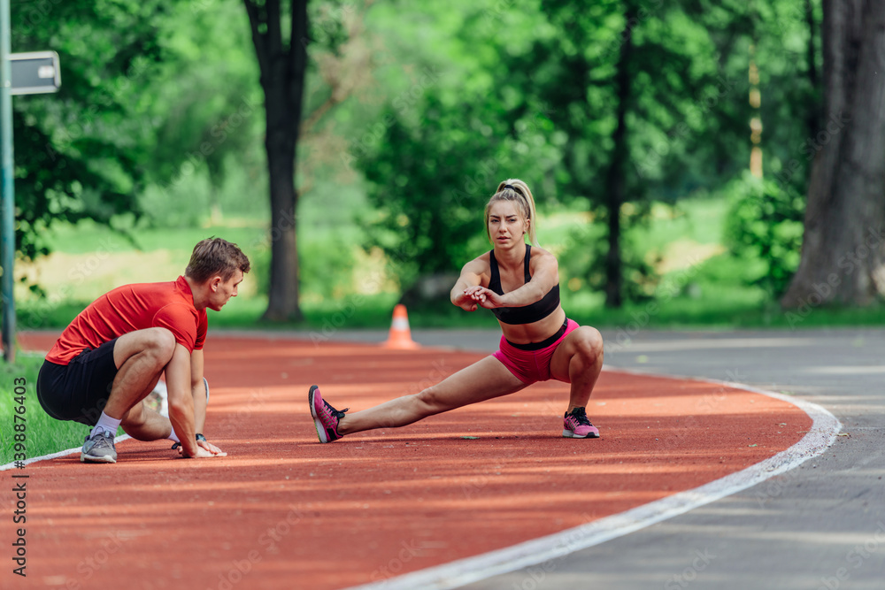 Young couple stretching before starting their morning jogging routine on a tartan track at the park.