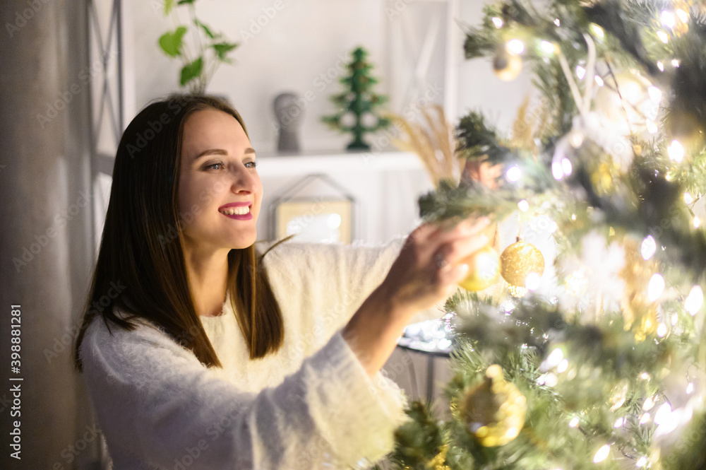 A young woman is decorating a Christmas tree at the evening. New Year preparing. Photo with grain