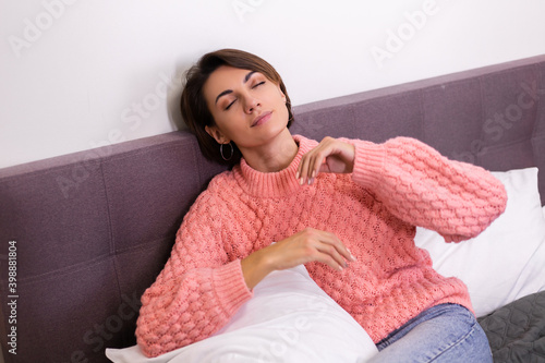 Caucasian pretty woman in pink cute knitted pullover resing at home in bed, smiling, enjoying time alone, hugging pillow.     photo