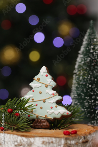 Gingerbread cookie in festive Christmas arrangement with bokeh lights in background. Biscuit in Christmas tree shape with royal icing.