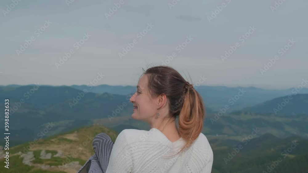 young girl with red hair in a white pullover on the top of a mountain, smiles and looks at a beautiful view. Shooting from behind. Blue sky, green forest. young girl with red hair in a white pullover on the top of a mountain, smiles and looks at a beautiful view. Shooting from behind. Blue sky, green forest.