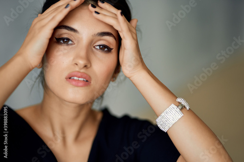 beautiful woman model touches her face with her hands on a gray background and evening dress decoration on her hand