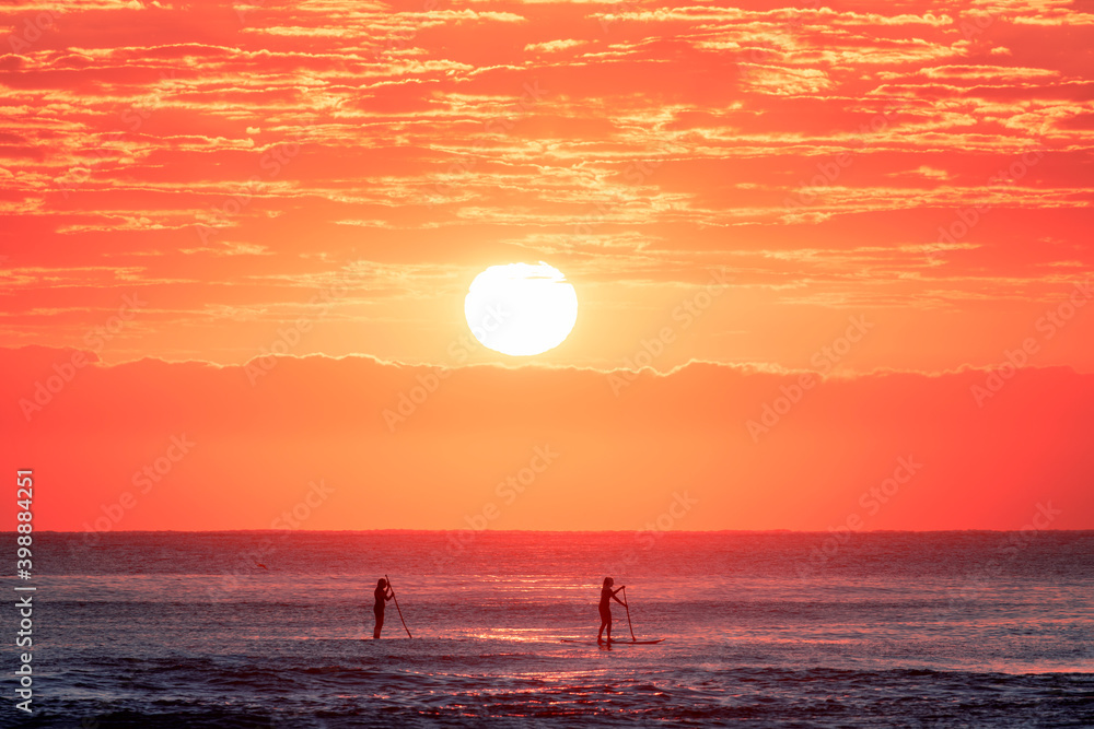 Stand up paddle boarders in the ocean with a colourful sunrise sky. Burleigh Heads, Gold Coast Australia