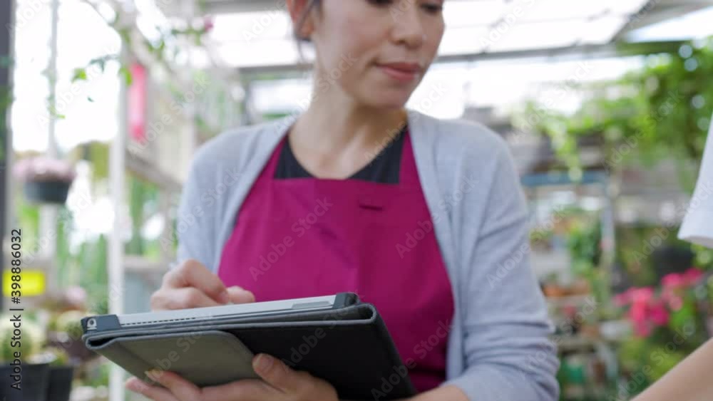 Asian and Caucesian gardener woman or business owner using computer tablet working together in greenhouse garden Asian and Caucesian gardener woman or business owner using computer tablet working together in greenhouse garden