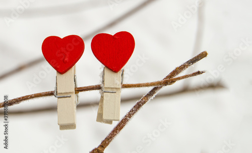 Two wooden clothespins with a red heart hang on a snow-covered branch, in winter, outdoors