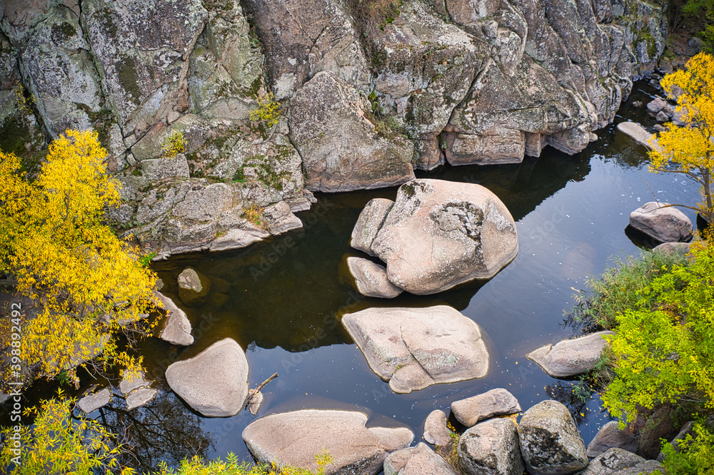 Fototapeta premium A picturesque stream flows in the Aktovsky Canyon, surrounded by autumn trees and large stone boulders